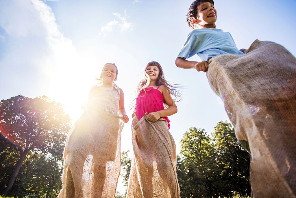 Low angle view of three happy children having fun in a sack race outdoors.